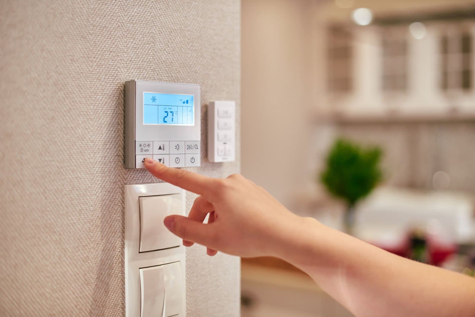 Doigt qui appuie sur un bouton d'un thermostat d'ambiance numérique fixé au mur