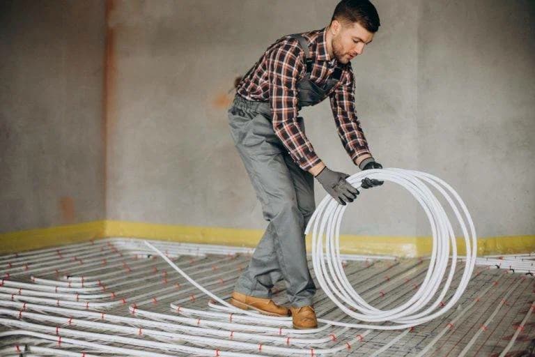 Man in geruit hemd die witte buizen voor vloerverwarming uitrolt over een isolatielaag